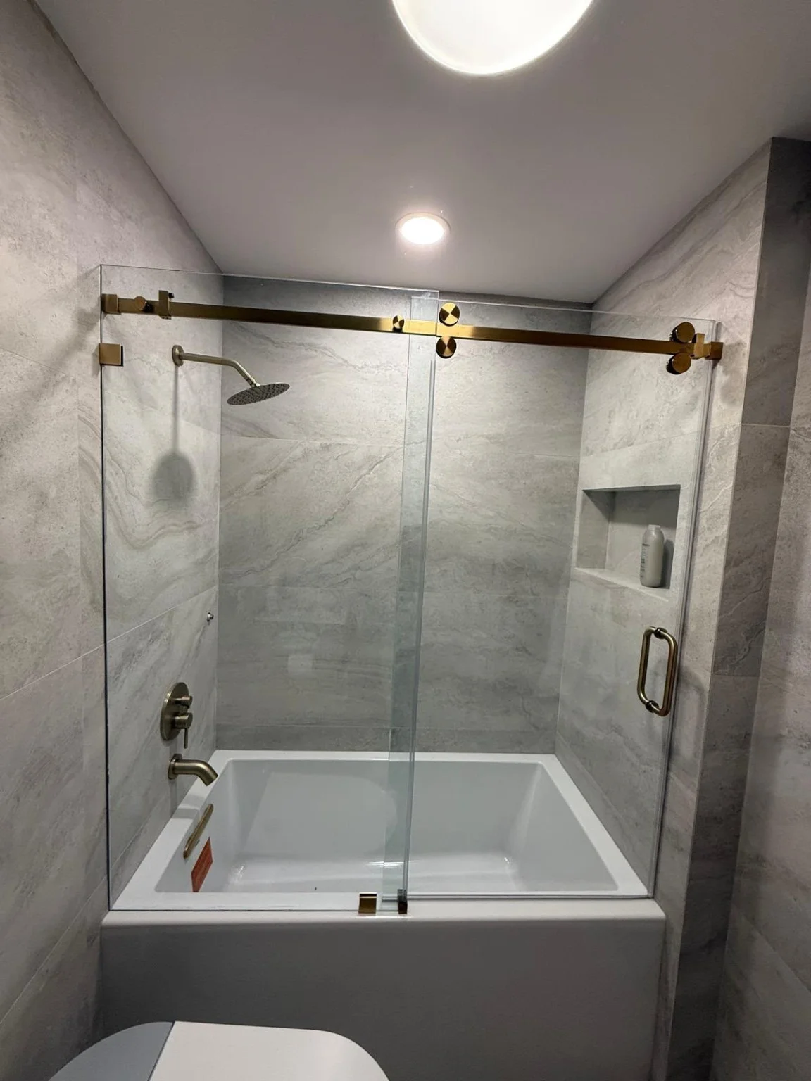 Glass bathtub enclosure and brass-tone hardware